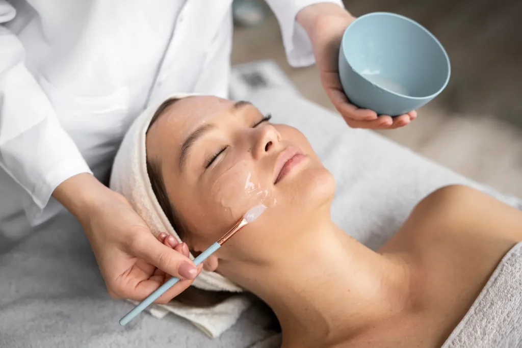 Close-up of a sophisticated beauty clinic menu board listing specialized facial treatments like Stem Cell and Aromatherapy facials. In the foreground, a sleek reception desk holds a bouquet of roses and high-end cosmetic jars, emphasizing a clean and professional medical spa environment.